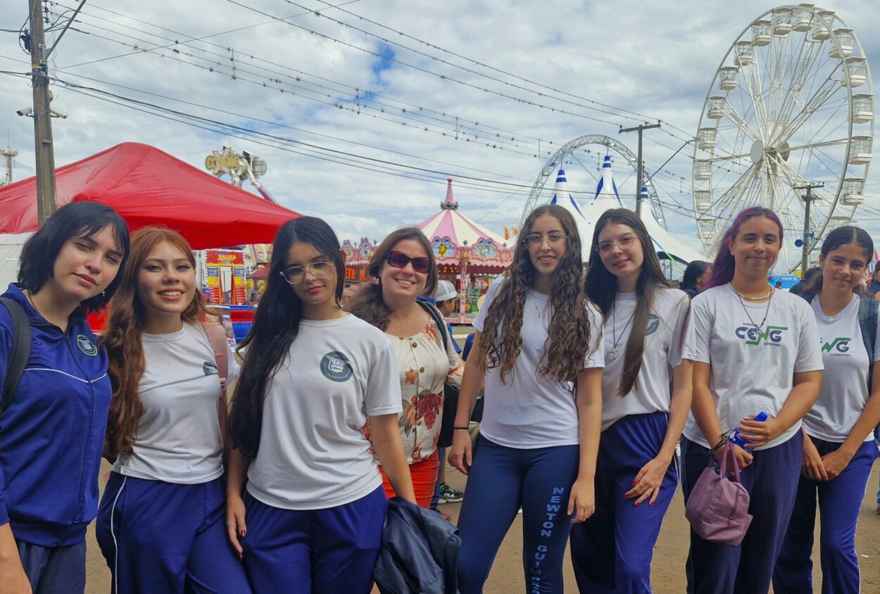 A imagem mostra as estudantes do clube Litterae Ludus acompanhadas da professora coordenadora, Franciela Zamariam. As alunas estão uniformizadas e ao fundo há um parque de diversões, uma das atrações da ExpoLondrina 2025.