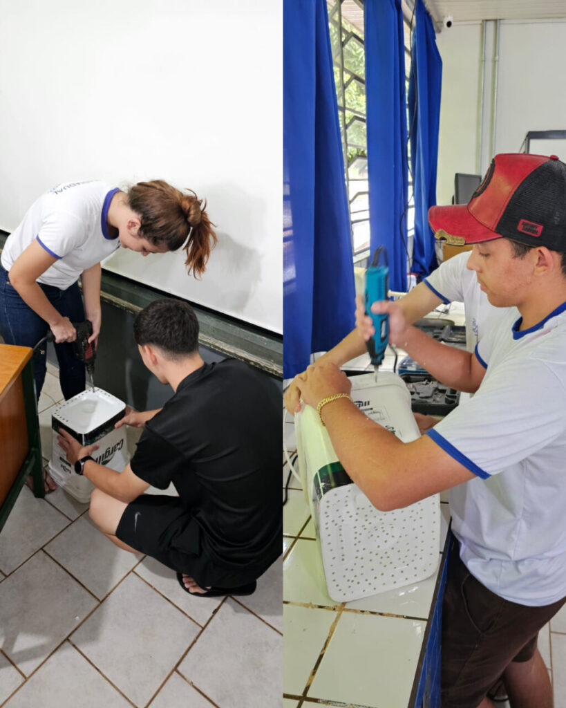 A imagem está dividida em duas partes e mostra estudantes envolvidos em uma atividade prática, possivelmente dentro de um projeto escolar voltado à sustentabilidade. À esquerda, uma aluna e um aluno trabalham juntos com uma furadeira elétrica para perfurar um balde branco reaproveitado. A atividade ocorre em uma sala com piso de cerâmica clara, próximo a uma parede branca com quadro negro. À direita, outro estudante também manuseia uma furadeira, concentrado em perfurar as laterais de um balde. Ele está em um ambiente escolar com janelas ao fundo, cortinas azuis e bancadas de azulejo branco. A atividade faz parte da construção de um sistema de compostagem incentivando o aprendizado prático e a conscientização ambiental.