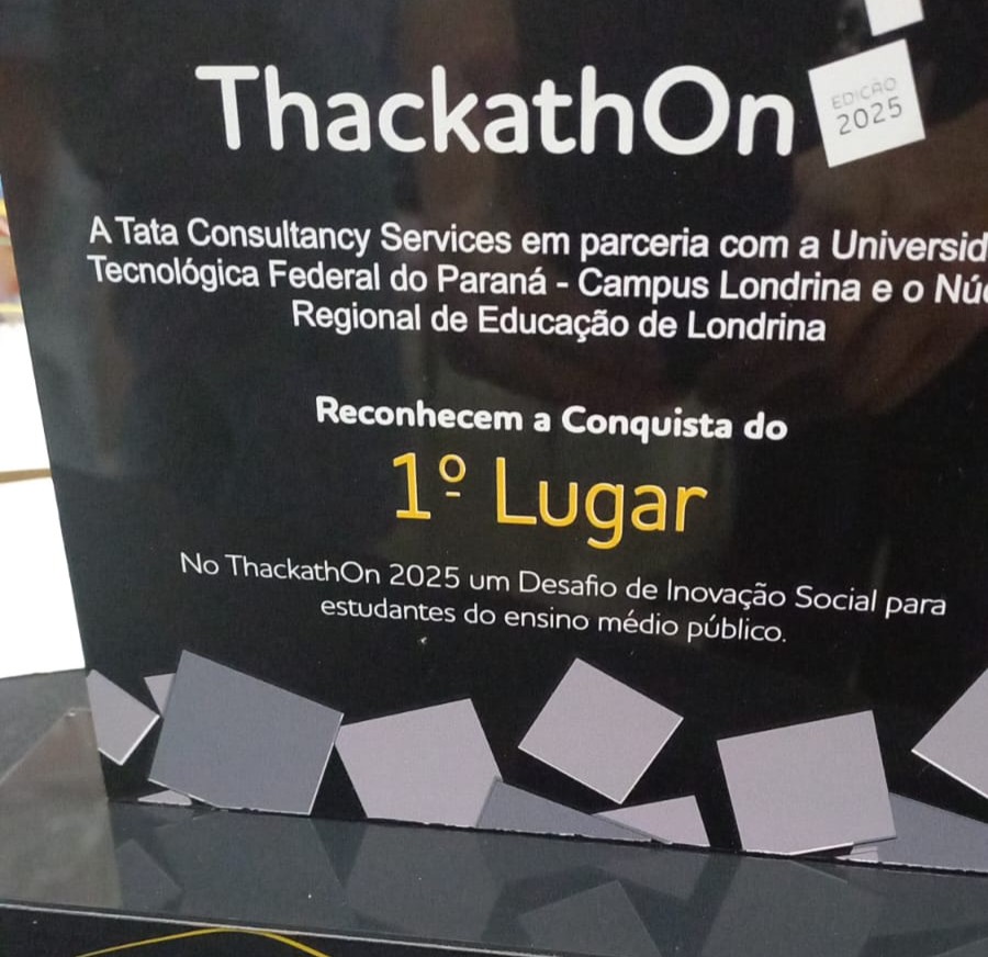 A imagem mostra um troféu com fundo preto e detalhes em cinza e amarelo. No topo está escrito "ThackathOn" em letras brancas, com um pequeno selo ao lado direito que diz “Edição 2025”. Abaixo, há o texto "A Tata Consultancy Services em parceria com a Universidade Tecnológica Federal do Paraná – Campus Londrina e o Núcleo Regional de Educação de Londrina reconhecem a conquista do 1º Lugar". A expressão “1º Lugar” está em destaque com fonte maior e na cor amarela. Logo abaixo, há mais um texto em branco: "No ThackathOn 2025 um Desafio de Inovação Social para estudantes do ensino médio público."