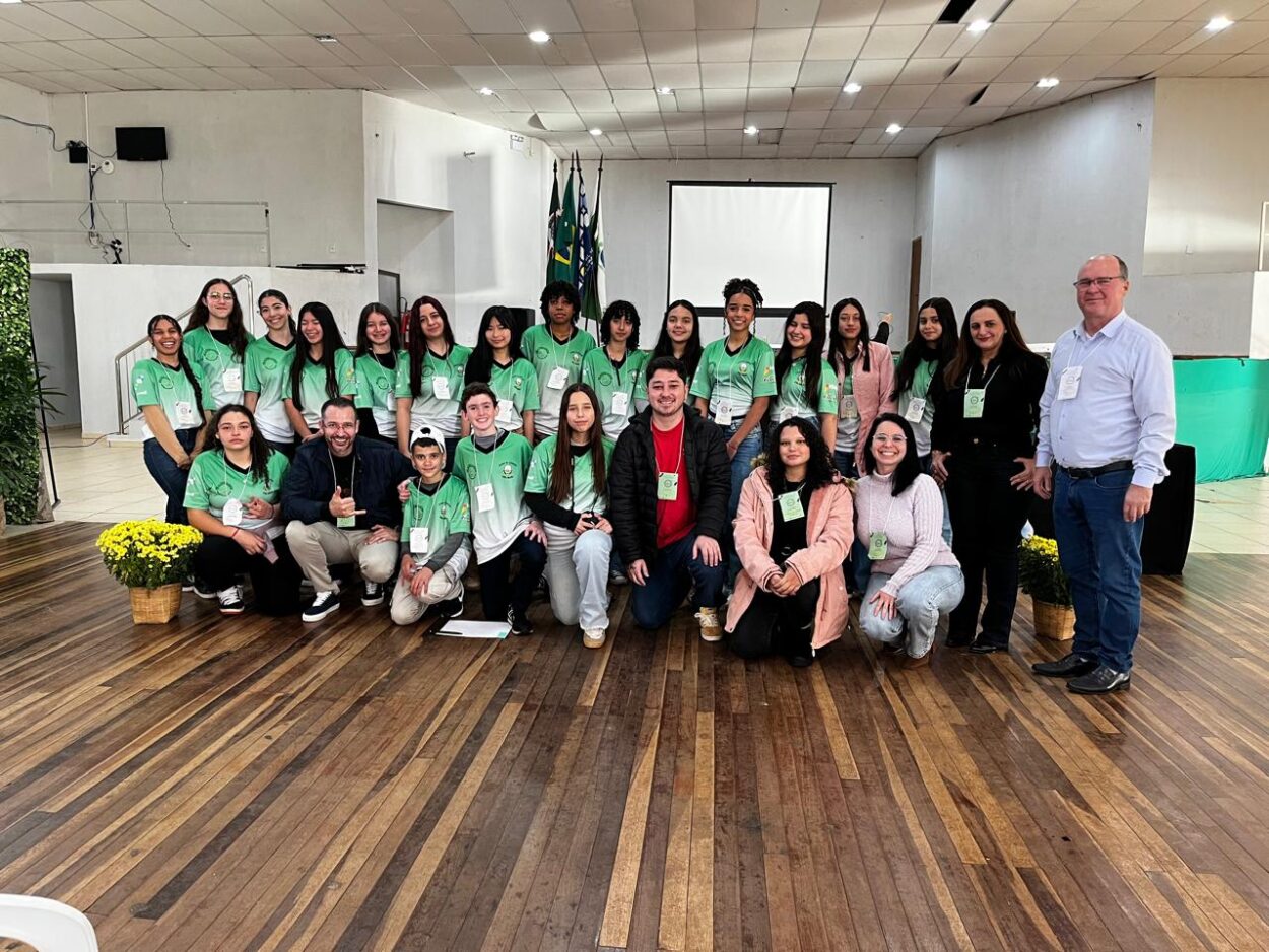 A imagem com fundo em um salão contendo a bandeira do Brasil no fundo, é possível ver em destaque as pessoas envolvidas no projeto, entre alunos bolsistas e professores na capa.