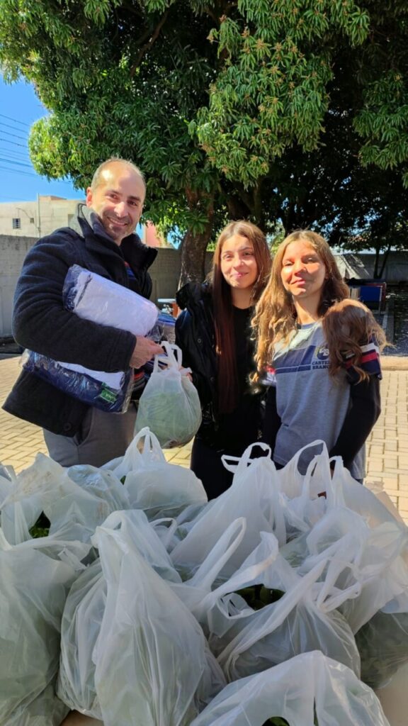 A galeria mostra fotos dos clubistas entregando as alfaces que eles cultivaram aos pais e alunos da escola. Há ambientes internos e externos e as alfaces estão envolvidas em sacolas plásticas para a praticidade no transporte. Alguns adultos são pais dos alunos e seguram pacotes contendo uniformes escolares.