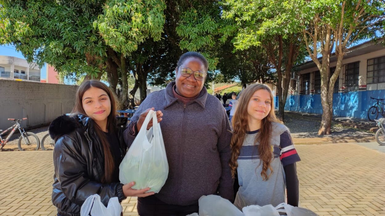 A galeria mostra fotos dos clubistas entregando as alfaces que eles cultivaram aos pais e alunos da escola. Há ambientes internos e externos e as alfaces estão envolvidas em sacolas plásticas para a praticidade no transporte. Alguns adultos são pais dos alunos e seguram pacotes contendo uniformes escolares.