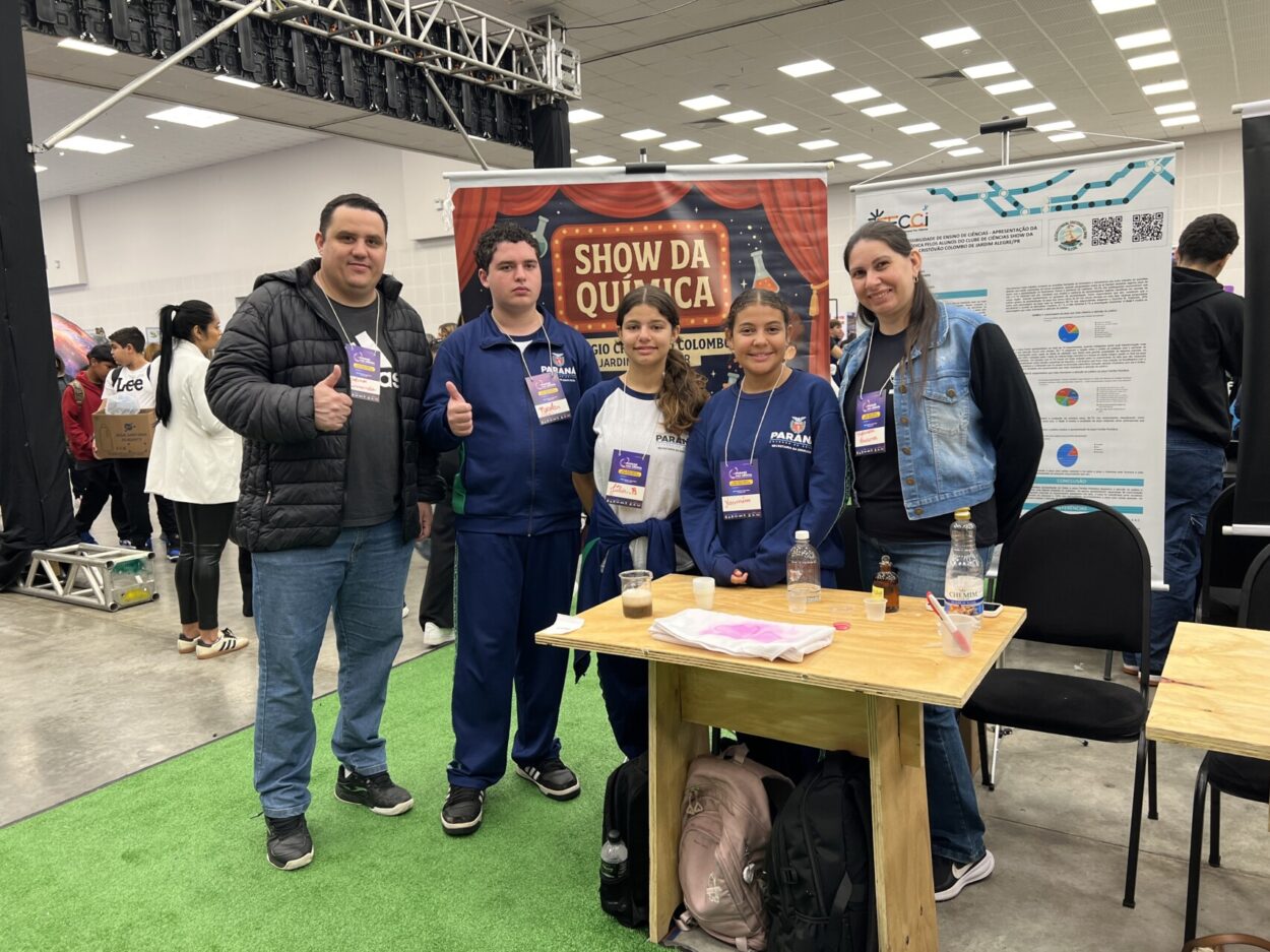 A primeira fotografia mostra um grupo formado por cinco estudantes e o professor, posando juntos em um evento científico. Eles estão em um ambiente de exposição, com pôsteres científicos ao fundo, que trazem textos e imagens relacionados a projetos escolares. Os estudantes vestem uniformes da rede estadual do Paraná. A segunda imagem é do Clube Show da Química. A imagem mostra um grupo de cinco pessoas, três estudantes e dois adultos, posando em um evento educacional. Eles estão em pé atrás de uma mesa de madeira com alguns materiais usados em experimentos, como garrafas plásticas com líquidos e copos descartáveis. O ambiente é um grande salão, bem iluminado, com outras pessoas, estandes e pôsteres ao fundo, reforçando o clima de evento científico. Na terceira fotografia tem um grupo formado por seis pessoas — quatro estudantes e dois adultos — posando juntos em um ambiente de feira científica. É o clube “Entre o passado e o presente, o que fica é a memória da gente”. Eles estão de pé atrás de uma mesa de madeira onde há várias fotos impressas que ilustram as atividades do projeto, incluindo imagens de grupos de alunos e de locais históricos. Ao fundo, há pôsteres científicos com o logotipo da Rede de Clubes Paraná Faz Ciência. A quarta imagem mostra quatro pessoas em um evento educacional, posando ao lado de uma mesa com materiais de um projeto sobre compostagem e reciclagem orgânica. Na frente, um jovem segura um balde verde identificado com o logotipo “C.C.H.E” e a imagem de uma minhoca, enquanto outro rapaz, ao lado, segura um copo transparente com um líquido escuro. No centro da mesa há um cesto com minhocas californianas e outro balde verde com ilustrações educativas relacionadas ao ciclo da compostagem. Atrás deles, uma moça e um homem adulto completam o grupo, todos usando crachás roxos de identificação do evento. A quinta imagem é do Clube Natureza em Perspectiva. A imagem mostra um grupo de estudantes posando para uma foto em um ambiente escolar ao ar livre. Ao todo, são cerca de vinte alunos, acompanhados por duas adultas, formando uma fileira de pé e outra agachada à frente. O grupo está em frente a um muro colorido e decorado com desenhos alegres, incluindo um sol, nuvens, flores e elementos da natureza.