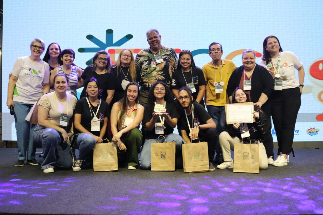 A primeira imagem é do Clube de Ciências ‘Robótica e Sustentabilidade, Solidariedade em Ação’ da Escola Estadual Professor Giampero Monacci de Itambé. A imagem mostra um grupo de pessoas reunidas sobre um palco, sorrindo e posando para a foto em um evento. Ao fundo, há um telão com logotipos coloridos e figuras ilustradas. A segunda imagem é do Clube Capivara’s Tech do Colégio Estadual Brasílio Itiberê. A imagem mostra um grupo de pessoas posando sorridentes sobre um palco, durante um evento. Ao fundo, há um telão com logotipos coloridos e desenhos estilizados, indicando um ambiente educacional. Na parte da frente, algumas pessoas estão agachadas, segurando certificados e sacolas de papel. Atrás delas, há outras pessoas, também sorrindo e comemorando. Na terceira fotografia do Clube CAPCiência do Colégio de Aplicação Pedagógica da UEM há um grupo de pessoas reunidas sobre um palco, sorrindo para a foto durante um evento. No centro, alguns participantes seguram uma bandeira verde e branca com o logotipo do “Capciência – Clube de Ciências”, que traz a ilustração de uma capivara. Atrás deles, há um grupo de adultos, todos usando crachás de identificação.