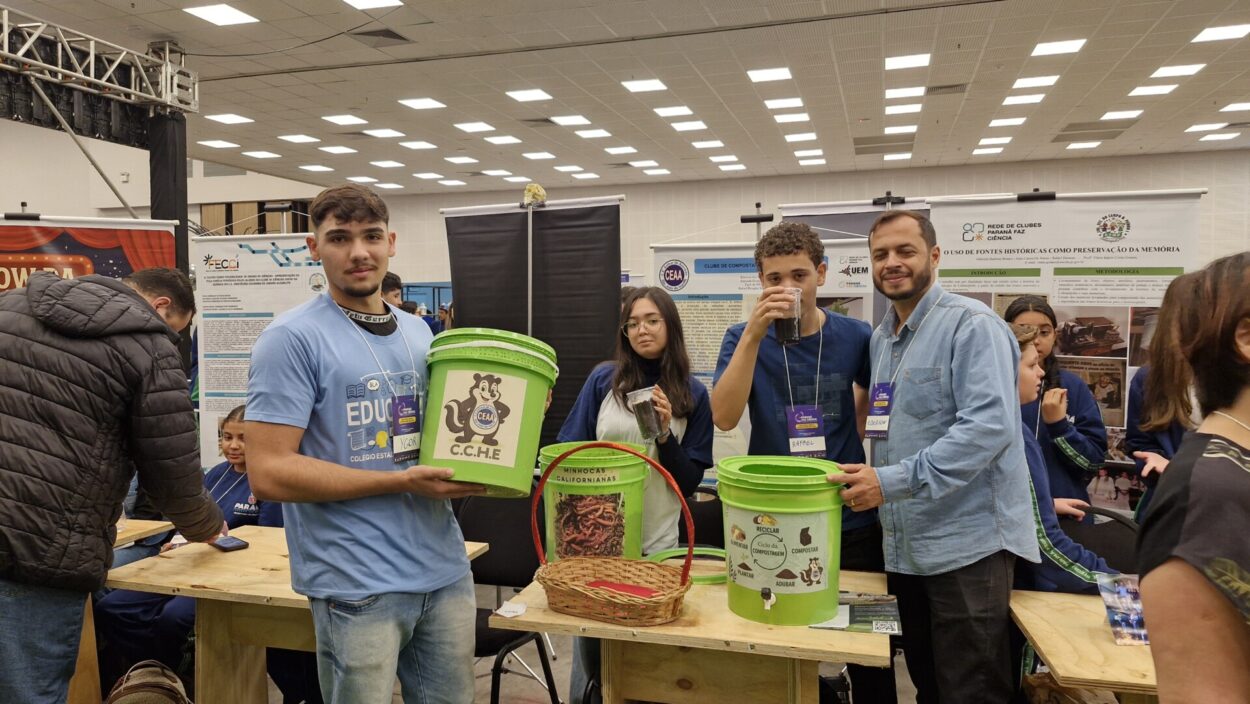 A primeira fotografia mostra um grupo formado por cinco estudantes e o professor, posando juntos em um evento científico. Eles estão em um ambiente de exposição, com pôsteres científicos ao fundo, que trazem textos e imagens relacionados a projetos escolares. Os estudantes vestem uniformes da rede estadual do Paraná. A segunda imagem é do Clube Show da Química. A imagem mostra um grupo de cinco pessoas, três estudantes e dois adultos, posando em um evento educacional. Eles estão em pé atrás de uma mesa de madeira com alguns materiais usados em experimentos, como garrafas plásticas com líquidos e copos descartáveis. O ambiente é um grande salão, bem iluminado, com outras pessoas, estandes e pôsteres ao fundo, reforçando o clima de evento científico. Na terceira fotografia tem um grupo formado por seis pessoas — quatro estudantes e dois adultos — posando juntos em um ambiente de feira científica. É o clube “Entre o passado e o presente, o que fica é a memória da gente”. Eles estão de pé atrás de uma mesa de madeira onde há várias fotos impressas que ilustram as atividades do projeto, incluindo imagens de grupos de alunos e de locais históricos. Ao fundo, há pôsteres científicos com o logotipo da Rede de Clubes Paraná Faz Ciência. A quarta imagem mostra quatro pessoas em um evento educacional, posando ao lado de uma mesa com materiais de um projeto sobre compostagem e reciclagem orgânica. Na frente, um jovem segura um balde verde identificado com o logotipo “C.C.H.E” e a imagem de uma minhoca, enquanto outro rapaz, ao lado, segura um copo transparente com um líquido escuro. No centro da mesa há um cesto com minhocas californianas e outro balde verde com ilustrações educativas relacionadas ao ciclo da compostagem. Atrás deles, uma moça e um homem adulto completam o grupo, todos usando crachás roxos de identificação do evento. A quinta imagem é do Clube Natureza em Perspectiva. A imagem mostra um grupo de estudantes posando para uma foto em um ambiente escolar ao ar livre. Ao todo, são cerca de vinte alunos, acompanhados por duas adultas, formando uma fileira de pé e outra agachada à frente. O grupo está em frente a um muro colorido e decorado com desenhos alegres, incluindo um sol, nuvens, flores e elementos da natureza.