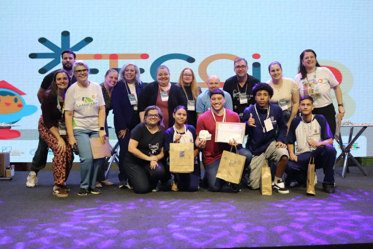 A primeira imagem é do Clube de Ciências Tenda Cultura Viva, do Colégio Estadual Professora Hilda Trautwein Kamal. Na foto há um grupo de pessoas reunidas sobre um palco, sorrindo e posando para a foto durante um evento. Ao fundo, há um telão sugerindo um encontro educacional. Os participantes estão lado a lado, segurando certificados, sacolas de papel e prêmios. Uma pessoa ao centro segura uma grande caixa de uma caixa de som JBL. Todos usam crachás de identificação e vestem roupas casuais. Na segunda fotografia vemos o Dengue Bot, do Colégio Estadual Vereador José Balan. Um grupo grande de pessoas reunidas sobre um palco, sorrindo para uma foto coletiva. Ao fundo, há um telão iluminado com elementos gráficos coloridos, sugerindo que o evento é de caráter educacional. Na parte da frente, alguns jovens seguram sacolas de papel e usam crachás de identificação e camisetas com o logotipo do Paraná. O Paisagismo Sustentável da Escola Estadual Manuel Bandeira, de Alto Piquiri, é a terceira foto. A imagem mostra um grupo numeroso de pessoas reunidas sobre um palco, posando para uma foto durante um evento educacional. Ao fundo, há um telão iluminado com elementos gráficos, reforçando o clima festivo e institucional. Na parte da frente, alguns jovens e adultos exibem certificados, troféus e prêmios. A quarta foto é do Clube Green Lab do Colégio Estadual Almirante Tamandaré, de Cruzeiro do Oeste. Na imagem é possível ver pessoas posando juntas em um palco. Há cerca de quinze pessoas, entre adultos e jovens, algumas agachadas na frente e outras em pé atrás. Os jovens na frente seguram certificados e sacolas de papel. No fundo, há um telão grande com um logotipo colorido.