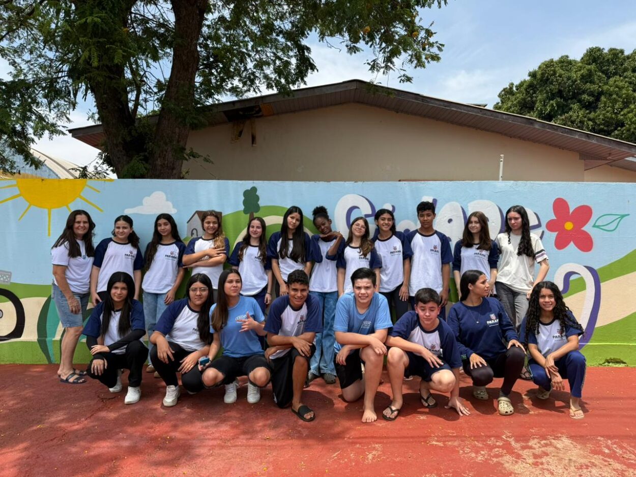 A primeira fotografia mostra um grupo formado por cinco estudantes e o professor, posando juntos em um evento científico. Eles estão em um ambiente de exposição, com pôsteres científicos ao fundo, que trazem textos e imagens relacionados a projetos escolares. Os estudantes vestem uniformes da rede estadual do Paraná. A segunda imagem é do Clube Show da Química. A imagem mostra um grupo de cinco pessoas, três estudantes e dois adultos, posando em um evento educacional. Eles estão em pé atrás de uma mesa de madeira com alguns materiais usados em experimentos, como garrafas plásticas com líquidos e copos descartáveis. O ambiente é um grande salão, bem iluminado, com outras pessoas, estandes e pôsteres ao fundo, reforçando o clima de evento científico. Na terceira fotografia tem um grupo formado por seis pessoas — quatro estudantes e dois adultos — posando juntos em um ambiente de feira científica. É o clube “Entre o passado e o presente, o que fica é a memória da gente”. Eles estão de pé atrás de uma mesa de madeira onde há várias fotos impressas que ilustram as atividades do projeto, incluindo imagens de grupos de alunos e de locais históricos. Ao fundo, há pôsteres científicos com o logotipo da Rede de Clubes Paraná Faz Ciência. A quarta imagem mostra quatro pessoas em um evento educacional, posando ao lado de uma mesa com materiais de um projeto sobre compostagem e reciclagem orgânica. Na frente, um jovem segura um balde verde identificado com o logotipo “C.C.H.E” e a imagem de uma minhoca, enquanto outro rapaz, ao lado, segura um copo transparente com um líquido escuro. No centro da mesa há um cesto com minhocas californianas e outro balde verde com ilustrações educativas relacionadas ao ciclo da compostagem. Atrás deles, uma moça e um homem adulto completam o grupo, todos usando crachás roxos de identificação do evento. A quinta imagem é do Clube Natureza em Perspectiva. A imagem mostra um grupo de estudantes posando para uma foto em um ambiente escolar ao ar livre. Ao todo, são cerca de vinte alunos, acompanhados por duas adultas, formando uma fileira de pé e outra agachada à frente. O grupo está em frente a um muro colorido e decorado com desenhos alegres, incluindo um sol, nuvens, flores e elementos da natureza.
