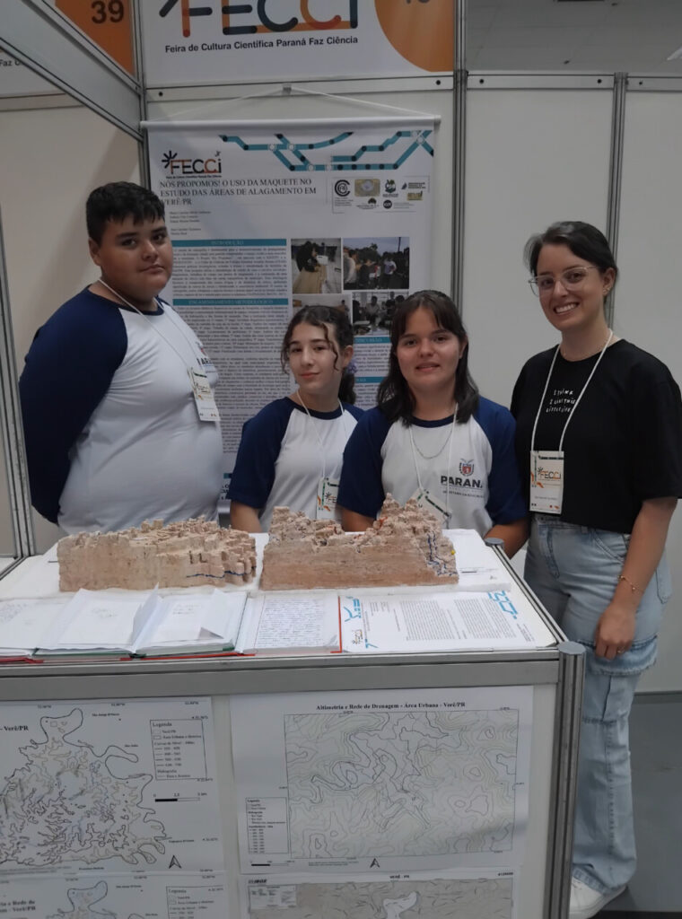 A galeria mostra 3 momentos do Clube de Ciências Aquavida na Feira de Cultura Científica Paraná Faz Ciência (FECCI). O ambiente é coberto e bem iluminado, com estandes e objetos para apresentação da pesquisa desenvolvida pelos clubistas. A última foto mostra o professor Samuel Moraes e os clubistas cujo projeto foi premiado na feira com o 3º lugar na categoria Desenvolvimento de Produtos Junior.