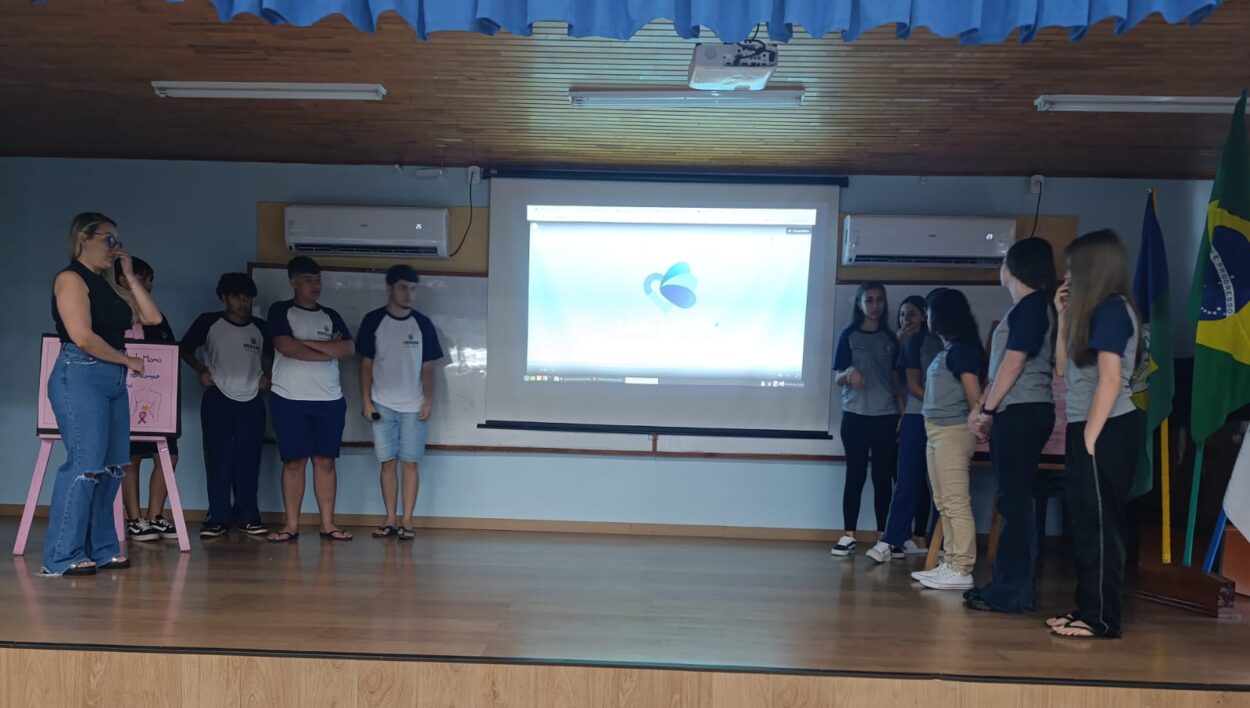 A galeria registra momentos da Culminância do Colégio Estadual Guilherme de Almeida, em Santa Izabel do Oeste (PR). Em um auditório com carteiras enfileiradas, palco, cortinas e projetor, professores e clubistas apresentam os projetos desenvolvidos ao longo do ano de 2025. Há, ainda, imagens de um panfleto intitulado 'Agrotóxicos e o Câncer de Mama' e outros momentos marcantes do clube.