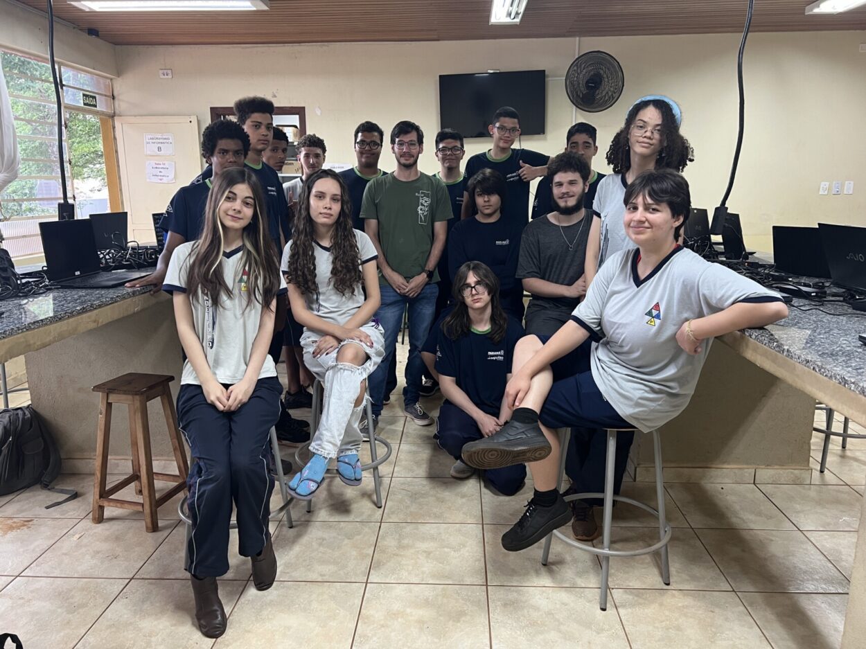 A foto é do Clube de Ciências ‘Makers CEUP” do Colégio Estadual Unidade Polo de Maringá. A imagem mostra um grupo de jovens reunidos em uma sala de aula que aparenta ser um laboratório de informática. Ao todo, há vários estudantes, em sua maioria adolescentes, organizados em duas fileiras. O ambiente possui bancadas de granito com computadores e monitores desligados, além de cabos e teclados sobre as mesas. Os estudantes vestem, em grande parte, camisetas de uniforme escolar em tons de cinza, azul e preto.