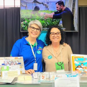 Débora Sant’Ana, articuladora do NAPI Paraná Faz Ciência, e a pesquisadora Edinalva Oliveira, no estande do NAPI Paraná Faz Ciência na Semana Araucária de CT&I, em Curitiba, junto de pesquisas desenvolvidas por clubes da rede (Foto/Marilaine Martins)