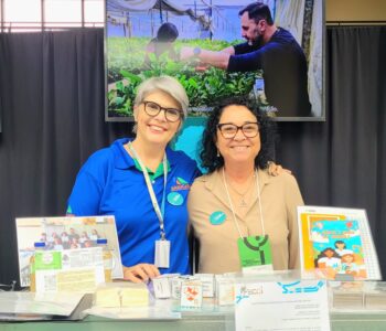 Débora Sant’Ana, articuladora do NAPI Paraná Faz Ciência, e a pesquisadora Edinalva Oliveira, no estande do NAPI Paraná Faz Ciência na Semana Araucária de CT&I, em Curitiba, junto de pesquisas desenvolvidas por clubes da rede (Foto/Marilaine Martins) 