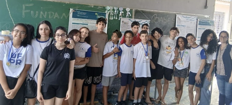 Grupo de estudantes posa para foto em sala de aula, ao lado de professora Andreia Petruy, após a apresentação dos trabalhos.