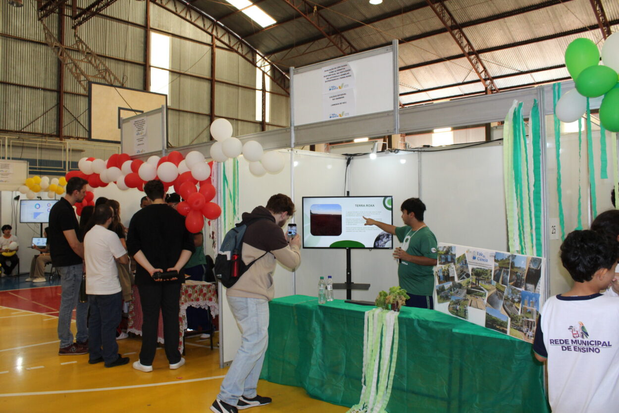 A galeria reúne momentos do 6º Vale da Ciência, feira promovida pela Universidade Federal do Paraná (UFPR) por meio do Câmpus Avançado de Jandaia do Sul. As imagens registram os estandes dos projetos dos clubes de ciências e seus autores em um pavilhão amplo, caracterizado por sua estrutura metálica aparente e pela iluminação natural que entra pelas laterais superiores.