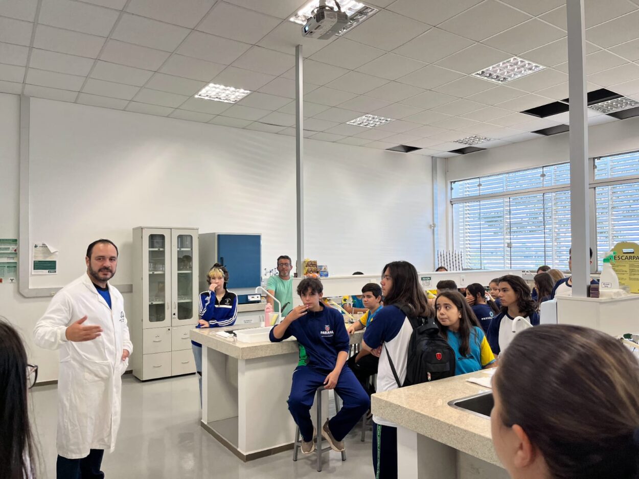 A galeria registra os momentos da visita do clube ao campus da UFFS Realeza. As imagens externas destacam a área verde da universidade e os estudantes acompanhados pelo coordenador do projeto durante a visita guiada. Já os registros internos apresentam as atividades práticas realizadas no laboratório, onde os alunos participaram da oficina.