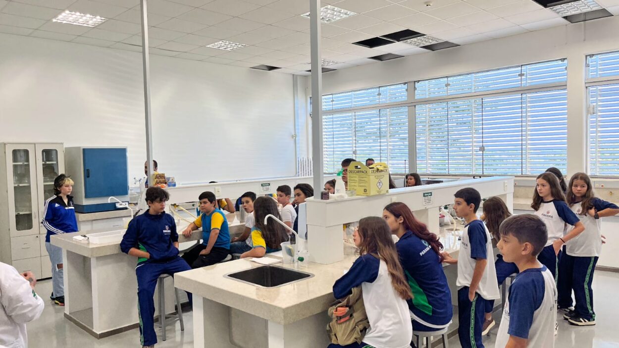 A galeria registra os momentos da visita do clube ao campus da UFFS Realeza. As imagens externas destacam a área verde da universidade e os estudantes acompanhados pelo coordenador do projeto durante a visita guiada. Já os registros internos apresentam as atividades práticas realizadas no laboratório, onde os alunos participaram da oficina.