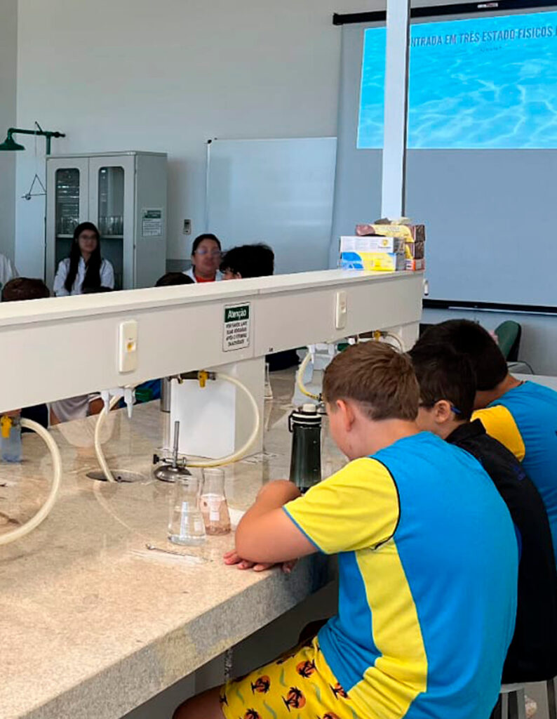 Momentos da Oficina Água realizada no laboratório da Universidade Federal da Fronteira Sul, campus Realeza. Nos detalhes, os alunos manuseando equipamentos como conta-gotas e as vidrarias de laboratório