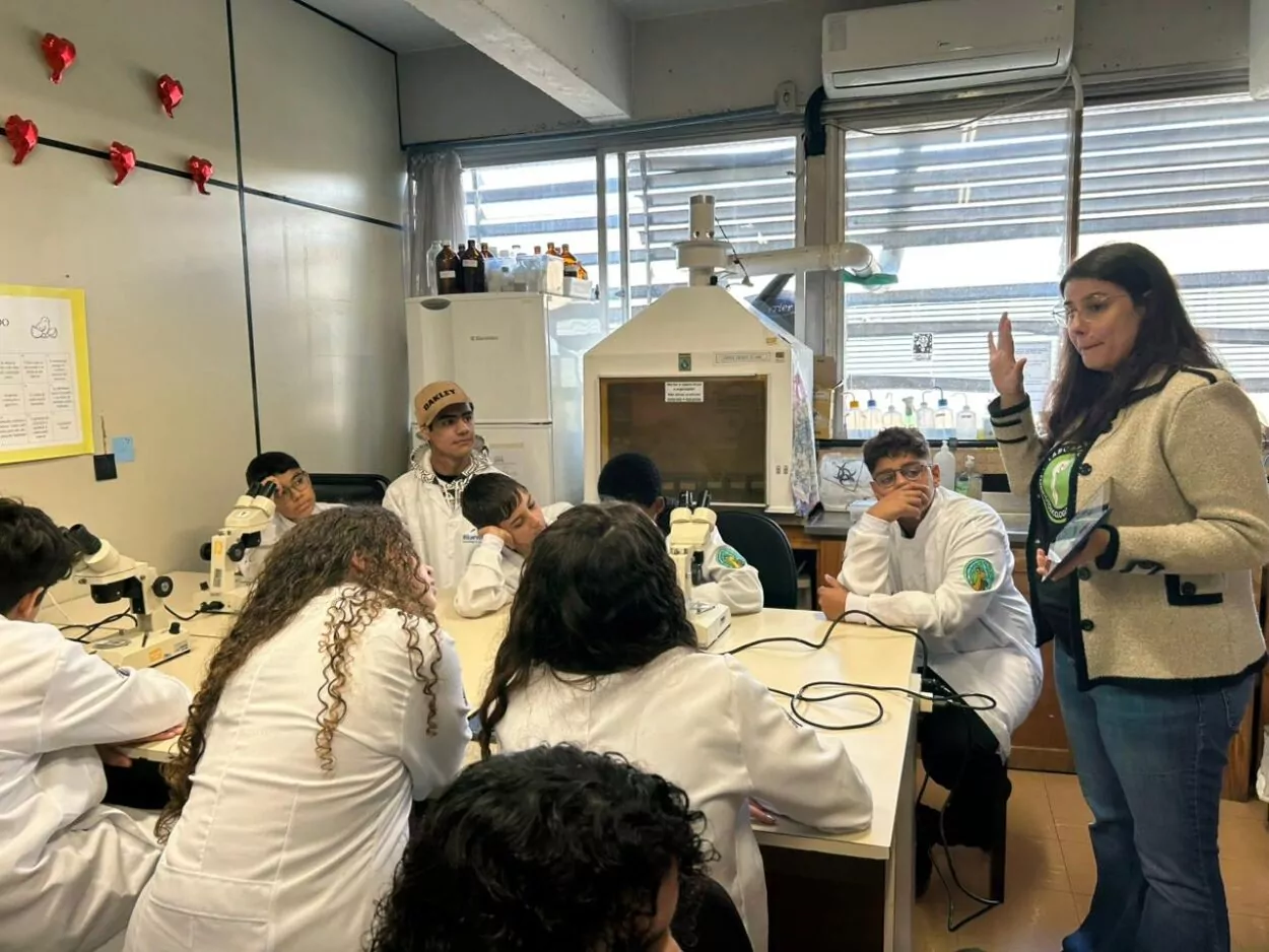 A galeria de fotos mostra momentos da visita dos clubistas à UFPR. Trata-se de ambientes fechados como um auditório e um laboratório. Há fotos da palestra que mostra várias cadeiras enfileiradas ocupadas por estudantes e professores, que estão assistindo à palestrante e à projeção de slide sobre o Rio iguaçu. Nas fotos do laboratório, mostra pequenos grupos de estudantes ouvindo orientações dos professores, usando microscópios e tablets, fazendo anotações. Todos estão vestindo jalecos com expressões de concentração e interesse.