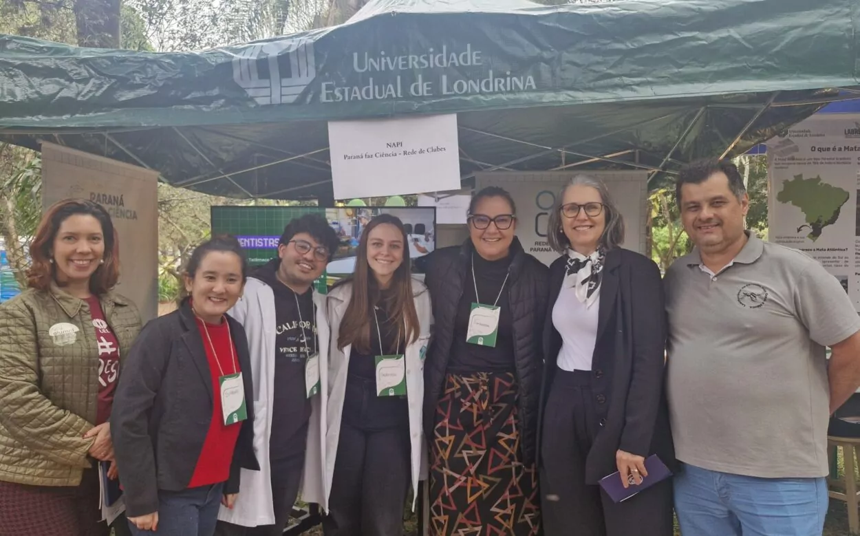 A imagem mostra a equipe NAPI UEL no estande do PRFC, localizado no Centro de Ciências Biológicas da UEL, durante a Feira das Profissões. Ao lado da equipe, está a Reitora da Universidade, professora Marta Favaro; a Chefe de Gabinete, professora Lisiane Freitas de Freitas; e o Diretor do CCB, professor João Zequi.