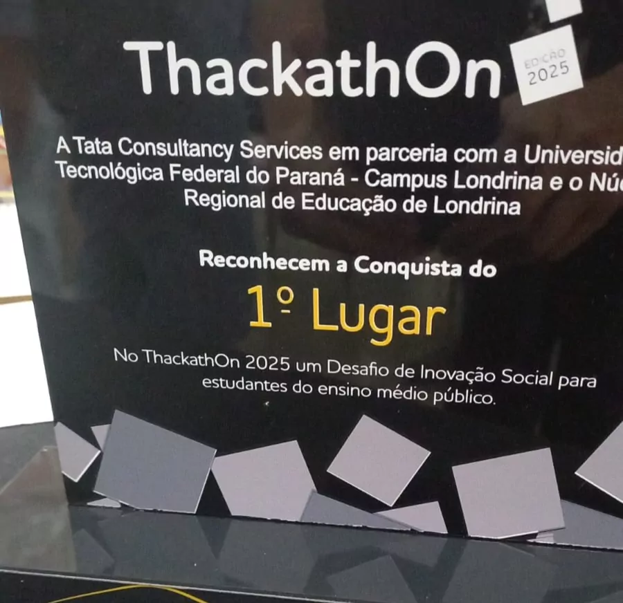 A imagem mostra um troféu com fundo preto e detalhes em cinza e amarelo. No topo está escrito "ThackathOn" em letras brancas, com um pequeno selo ao lado direito que diz “Edição 2025”. Abaixo, há o texto "A Tata Consultancy Services em parceria com a Universidade Tecnológica Federal do Paraná – Campus Londrina e o Núcleo Regional de Educação de Londrina reconhecem a conquista do 1º Lugar". A expressão “1º Lugar” está em destaque com fonte maior e na cor amarela. Logo abaixo, há mais um texto em branco: "No ThackathOn 2025 um Desafio de Inovação Social para estudantes do ensino médio público."