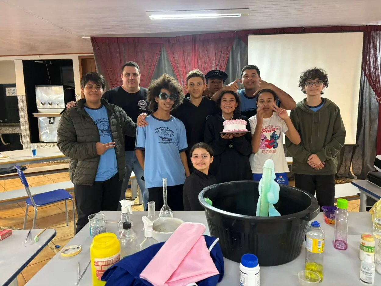 A galeria é composta por cinco fotografias, retratando diferentes momentos de atividades escolares desenvolvidas pelos Clubes de Ciências. A primeira foto expõe um grupo de estudantes e um professor posicionados atrás de três composteiras verdes com etiquetas, em um projeto que aborda o reaproveitamento de resíduos orgânicos. A segunda foto mostra alunos e professores posando ao redor de uma bancada com frascos, reagentes e uma grande bacia. A cena remete a um experimento de ciências em andamento, demonstrando práticas laboratoriais e espírito de equipe. Na terceira fotografia há um grupo de estudantes apresentando o projeto do Clube de Ciências “Entre o passado e o presente, o que fica é a memória da gente”. A exposição conta com objetos antigos e decoração com fitas coloridas, promovendo uma reflexão sobre a memória. A quarta foto mostra os alunos participando de uma atividade interativa sobre reciclagem, utilizando caixas organizadas por tipo de resíduo (plástico, papel, etc.). Crianças observam e manuseiam objetos, aprendendo sobre o descarte correto de materiais. Na última foto há dois alunos que apresentam um painel, ao lado de caixas de coleta seletiva. Uma aluna observa o espaço, que contém cartazes e materiais ligados à preservação ambiental.