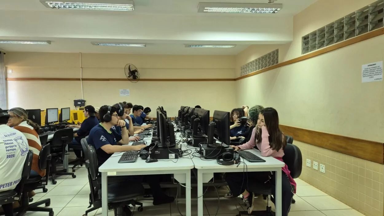 A imagem é uma galeria composta por seis fotografias, que retratam atividades desenvolvidas por diferentes grupos escolares ligados a Clubes de Ciências. A primeira foto tem um grupo de alunos sorrindo. O grupo está sentado em um ambiente interno decorado com plantas em prateleiras e cartazes. A segunda imagem mostra uma sala de informática com vários estudantes sentados em frente a computadores de mesa. Eles estão organizados em duas fileiras, cada uma voltada para o centro da sala, com monitores, teclados e fones de ouvido disponíveis. A maioria dos alunos parecem estar concentrados nas telas, digitando ou usando os fones. A sala tem iluminação fluorescente, paredes claras e alguns avisos afixados. Ao fundo, há ventiladores de parede e janelas com blocos de vidro para ventilação. O ambiente transmite uma atmosfera de estudo. A terceira fotografia tem alunos e visitantes interagindo em uma bancada comprida, realizando atividades práticas e experimentos. Há papéis com explicações e materiais sobre a mesa, indicando uma exposição interativa. A quarta foto mostra várias pessoas observando atentamente uma exposição de trabalhos em um espaço decorado com tecido verde. Na quinta foto tem um grupo de alunos apresentando um projeto do Clube de Ciências em uma sala decorada com folhas verdes penduradas. Na frente da mesa, há cartazes escritos e materiais como garrafas PET e experimentos. Na última foto há um grupo de estudantes, alguns vestidos com roupas típicas de festa junina, participando de uma atividade que envolve códigos QR. Uma das alunas segura um cartaz com o título “Quiz da ciência”, sugerindo uma abordagem lúdica para aprender conteúdos científicos.