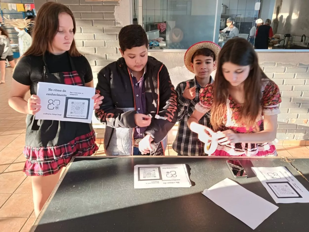 A imagem é uma galeria composta por seis fotografias, que retratam atividades desenvolvidas por diferentes grupos escolares ligados a Clubes de Ciências. A primeira foto tem um grupo de alunos sorrindo. O grupo está sentado em um ambiente interno decorado com plantas em prateleiras e cartazes. A segunda imagem mostra uma sala de informática com vários estudantes sentados em frente a computadores de mesa. Eles estão organizados em duas fileiras, cada uma voltada para o centro da sala, com monitores, teclados e fones de ouvido disponíveis. A maioria dos alunos parecem estar concentrados nas telas, digitando ou usando os fones. A sala tem iluminação fluorescente, paredes claras e alguns avisos afixados. Ao fundo, há ventiladores de parede e janelas com blocos de vidro para ventilação. O ambiente transmite uma atmosfera de estudo. A terceira fotografia tem alunos e visitantes interagindo em uma bancada comprida, realizando atividades práticas e experimentos. Há papéis com explicações e materiais sobre a mesa, indicando uma exposição interativa. A quarta foto mostra várias pessoas observando atentamente uma exposição de trabalhos em um espaço decorado com tecido verde. Na quinta foto tem um grupo de alunos apresentando um projeto do Clube de Ciências em uma sala decorada com folhas verdes penduradas. Na frente da mesa, há cartazes escritos e materiais como garrafas PET e experimentos. Na última foto há um grupo de estudantes, alguns vestidos com roupas típicas de festa junina, participando de uma atividade que envolve códigos QR. Uma das alunas segura um cartaz com o título “Quiz da ciência”, sugerindo uma abordagem lúdica para aprender conteúdos científicos.