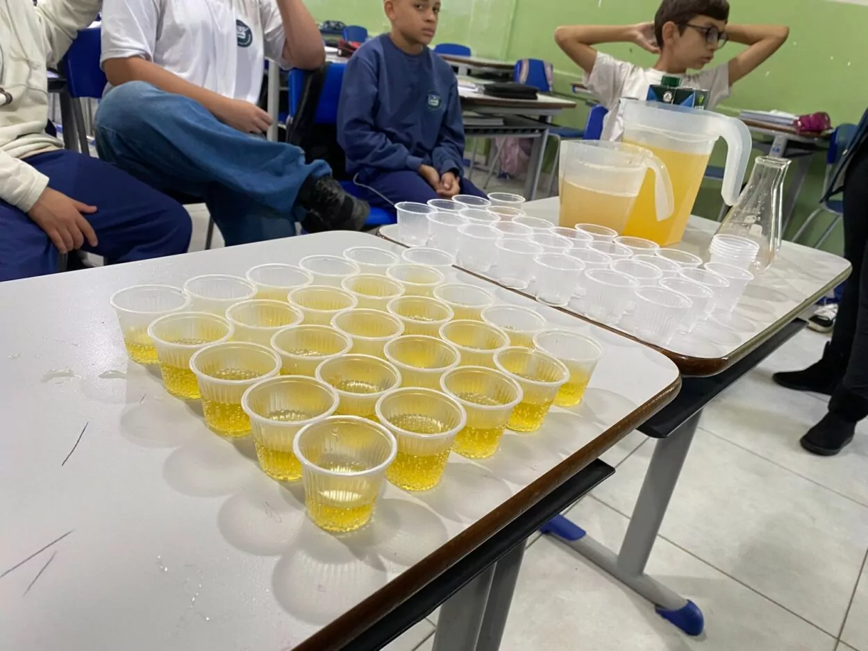 A galeria de fotos mostra momentos da apresentação e degustação do energético produzido pelo clube de ciências Ciência na Mesa. As imagens mostram estudantes na sala de aula com as mesas organizadas para oferecer o energético em copo descartáveis. Todos parecem felizes, sorrindo e curiosos com a proposta de bebida alternativa