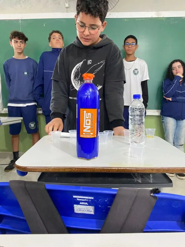 A galeria de fotos mostra momentos da apresentação e degustação do energético produzido pelo clube de ciências Ciência na Mesa. As imagens mostram estudantes na sala de aula com as mesas organizadas para oferecer o energético em copo descartáveis. Todos parecem felizes, sorrindo e curiosos com a proposta de bebida alternativa