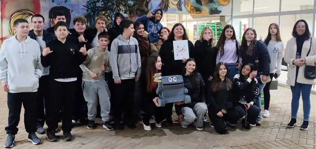 A foto mostra 22 pessoas, entre elas, os clubistas do Pilha nas Abelhas após suas apresentações no 8º MIPEEC, que posam para foto. A professora segura a logo do colégio e outras duas pessoas seguram o Robô Papa-Pilhas