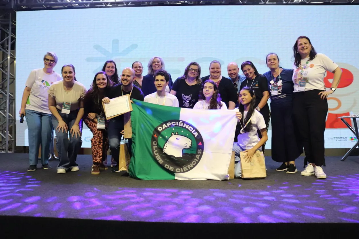 A primeira imagem é do Clube de Ciências ‘Robótica e Sustentabilidade, Solidariedade em Ação’ da Escola Estadual Professor Giampero Monacci de Itambé. A imagem mostra um grupo de pessoas reunidas sobre um palco, sorrindo e posando para a foto em um evento. Ao fundo, há um telão com logotipos coloridos e figuras ilustradas. A segunda imagem é do Clube Capivara’s Tech do Colégio Estadual Brasílio Itiberê. A imagem mostra um grupo de pessoas posando sorridentes sobre um palco, durante um evento. Ao fundo, há um telão com logotipos coloridos e desenhos estilizados, indicando um ambiente educacional. Na parte da frente, algumas pessoas estão agachadas, segurando certificados e sacolas de papel. Atrás delas, há outras pessoas, também sorrindo e comemorando. Na terceira fotografia do Clube CAPCiência do Colégio de Aplicação Pedagógica da UEM há um grupo de pessoas reunidas sobre um palco, sorrindo para a foto durante um evento. No centro, alguns participantes seguram uma bandeira verde e branca com o logotipo do “Capciência – Clube de Ciências”, que traz a ilustração de uma capivara. Atrás deles, há um grupo de adultos, todos usando crachás de identificação.