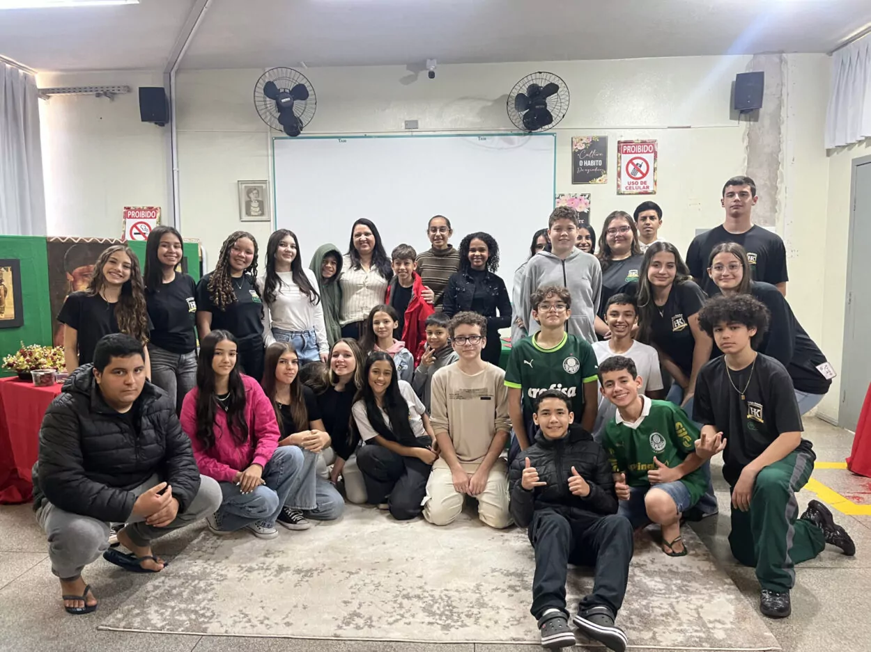 Na primeira fotografia é possível ver um grupo de pessoas posando juntas dentro de uma sala de aula. Ao todo, são dez pessoas: oito jovens e dois adultos. Eles estão posicionados lado a lado. O ambiente é típico de sala de aula, com paredes amarelas, quadro verde ao fundo e piso de cerâmica. A segunda imagem é do Clube Ilha da Ciência. A imagem mostra um grupo de estudantes e duas mulheres posando em um ambiente ao ar livre, com árvores, arbustos e canteiros de horta ao fundo. O grupo está sorridente, alguns em pé e outros agachados na frente. Na terceira fotografia tem um grupo de estudantes reunidos em um ambiente escolar ao ar livre, em frente a um jardim vertical com diversas plantas verdes. Eles estão distribuídos em pé e agachados, posando para a foto. A quarta imagem mostra um grupo de estudantes e um adulto reunidos em um espaço ao ar livre, posando para uma foto em frente a uma grande escultura de uma figura humana com os braços abertos. O grupo está distribuído sobre um pequeno morro coberto de grama, alguns sentados e outros em pé. A quinta imagem é do Clube Experimentando a Ciência: Descobrindo cores e novos sabores. A imagem mostra um grupo de estudantes e professores posando para uma foto ao ar livre, em frente a uma placa de madeira com o desenho de uma abelha e a palavra “Meliponário”. Estão sorridentes e organizados ao redor da placa. Na sexta imagem mostra um grupo grande de pessoas, formado por adolescentes e um adulto, posando para uma foto em uma sala. Eles estão organizados em duas fileiras: alguns sentados ou agachados na frente. A sala tem paredes claras, ventiladores fixados na parede e um quadro branco ao fundo. À esquerda, há uma mesa com uma toalha vermelha e alguns objetos decorativos para um evento escolar. A última fotografia tem um grupo de estudantes e alguns adultos reunidos para uma foto em um ambiente escolar externo. Eles estão em frente a uma parede branca com detalhes verdes e uma janela comprida com grades. O grupo está posicionado em duas fileiras, com alguns agachados na frente e outros em pé atrás, todos sorrindo.