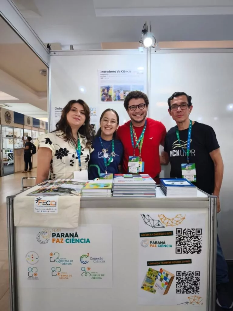 Integrantes da equipe do Paraná Faz Ciência posam para foto no estande do projeto durante o 36º Congresso Brasileiro de Zoologia (CBZ) e a 3ª Conferência da Zoologia na Indústria (CIZOO). Entre eles está o professor Rodrigo Arantes Reis. O grupo está atrás de um balcão expositivo com livros e materiais de divulgação científica. No painel do estande aparecem também informações e QR codes para acesso a conteúdos e projetos vinculados ao programa, que promove a integração entre pesquisa, educação e sociedade.
